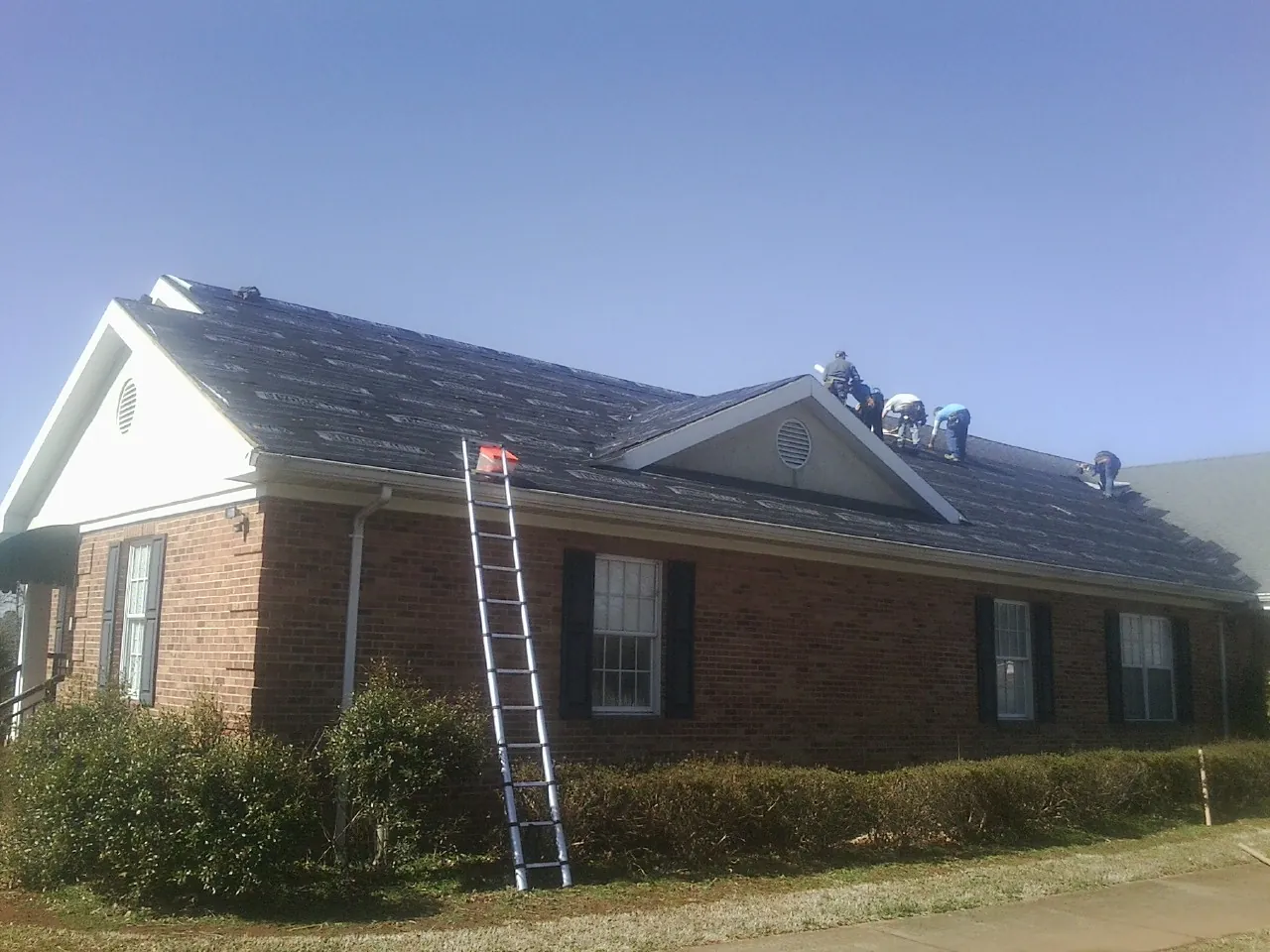 Crew tearing shingles off a brick ranch roof with a ladder set — Metal Roof Repair work by our crew in Dennison