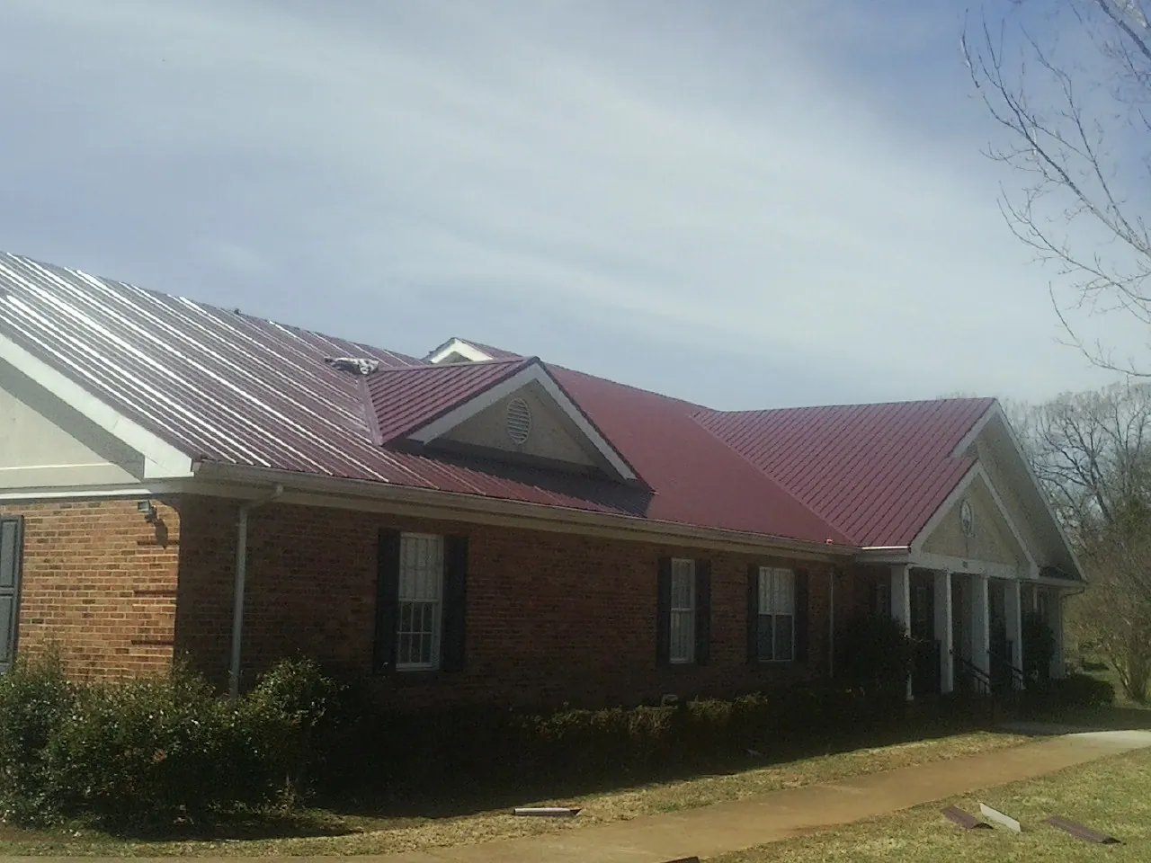 Red metal roof with gabled entries on a long brick building, from a Hail Damage Roof Repair job in Dennison