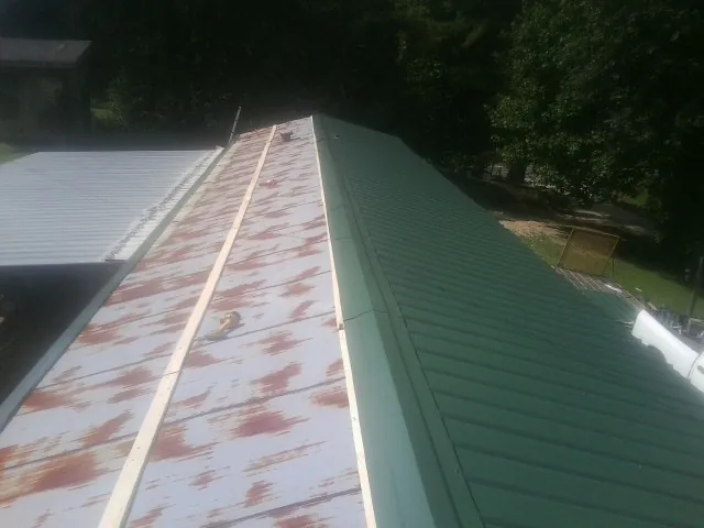 Old rusted panels beside newly installed green metal roofing — Wind Damage Roof Repair by Roofing Brothers in Dennison