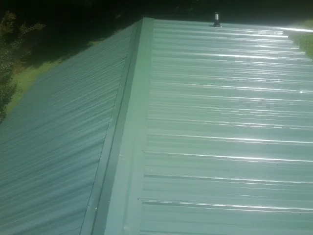 New green metal panels meeting at the ridge of a roof — Flat Roof Repair work by our crew in Dennison