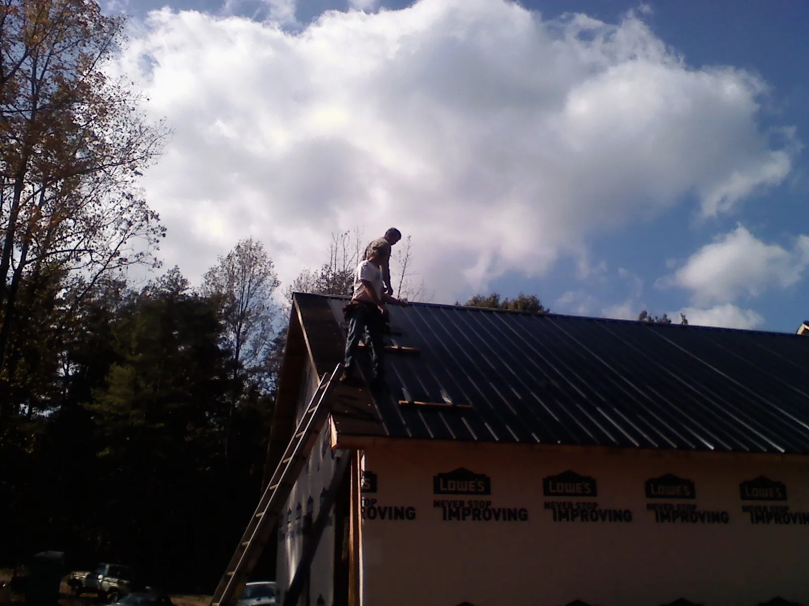 Roofer fastening dark metal panels high against a cloudy sky, from a Roof Inspection job in Dennison