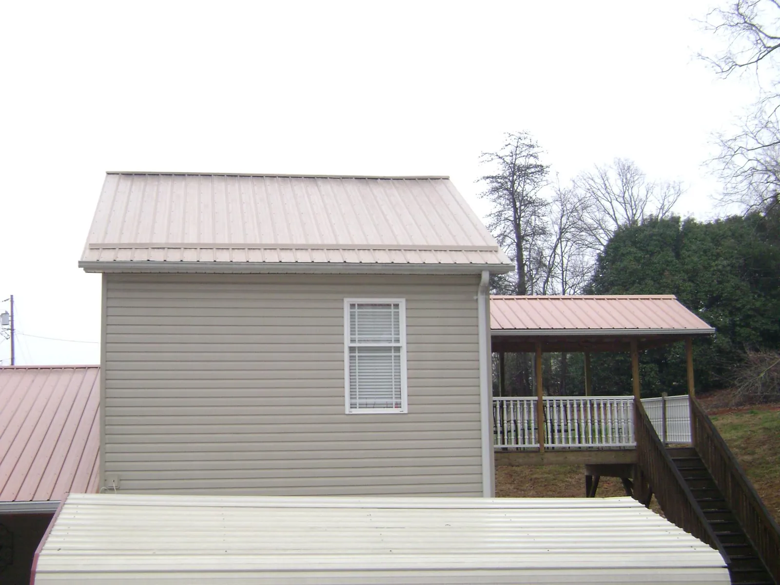 Tan metal roofs on a two story addition and attached porch, from a Roof Replacement job in Dennison